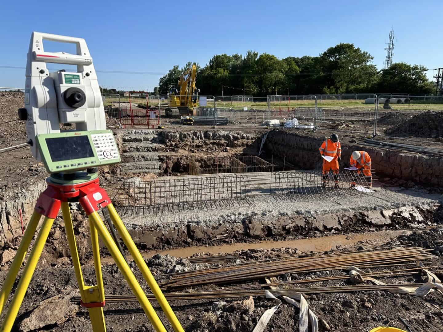 Surveying equipment on a construction site with workers and machinery.