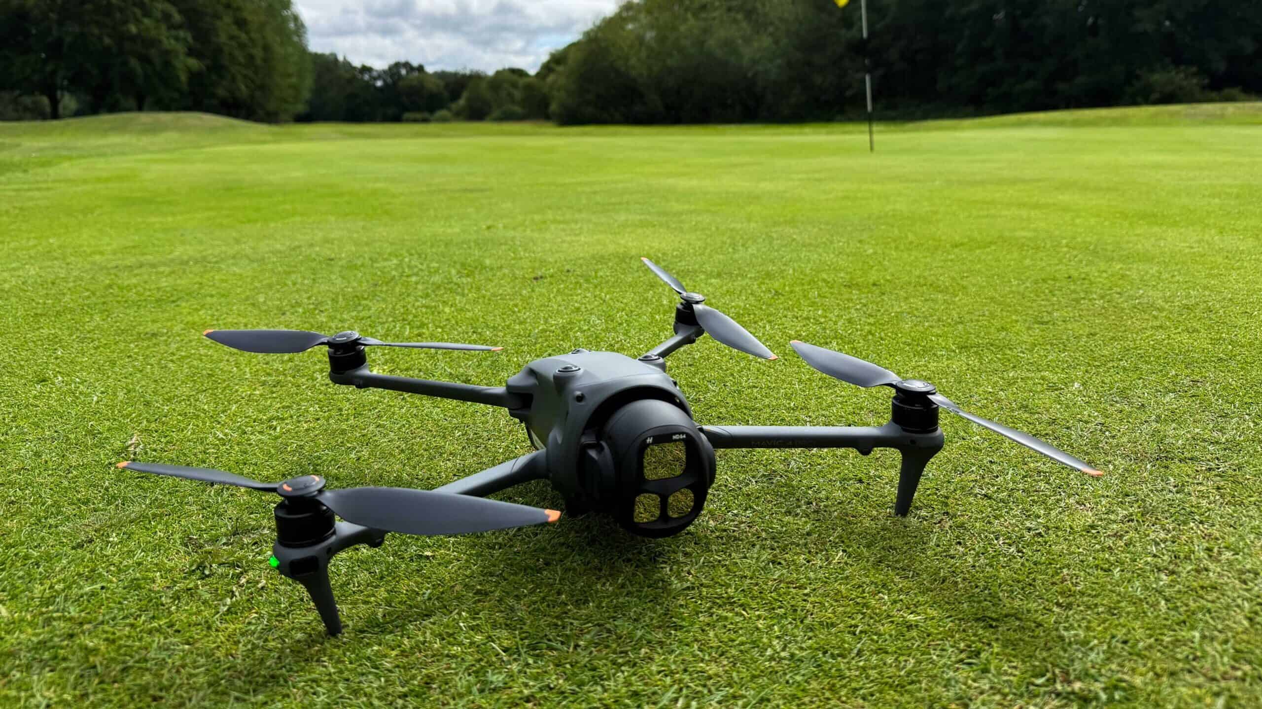 Quadcopter drone flying over a golf course with green grass and trees.